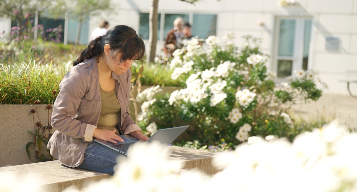 student looks down at laptop sitting on Gateway campus rooftop patio